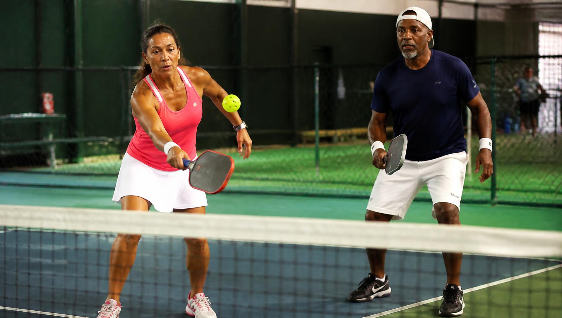Two players mid-rally on an indoor pickleball court